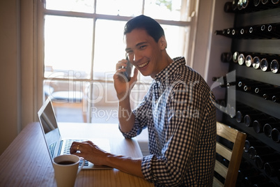 Man using laptop while talking on mobile phone