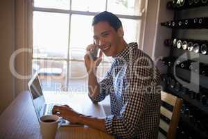 Man using laptop while talking on mobile phone