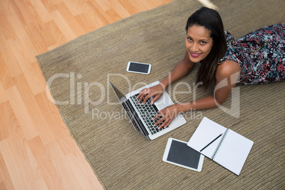 Female executive using laptop while lying on carpet in the office