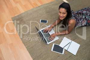 Female executive using laptop while lying on carpet in the office