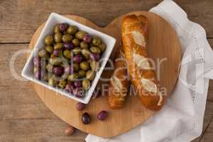 Overhead view of olives and bread on heart shape cutting board