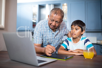 Man writing on tablet while using laptop with grandson