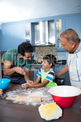 Happy father sprinkling flour on son hand while preparing food with grandfather