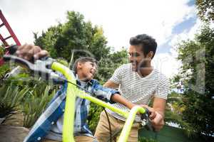 Happy father assisting son while riding bicycle