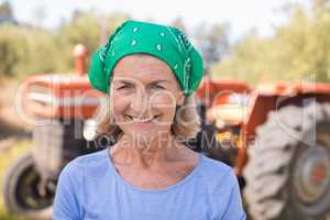 Portrait of happy woman standing against tractor in olive farm