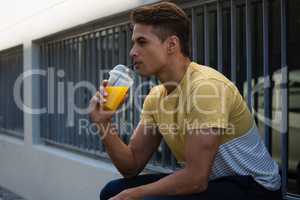 Young man drinking juice by wall in city