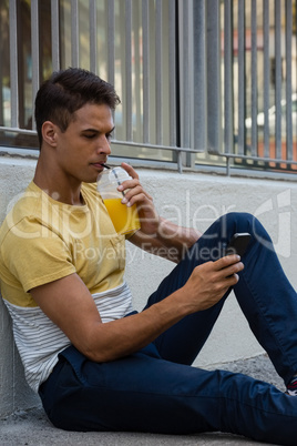 Young man having drink while using mobile phone
