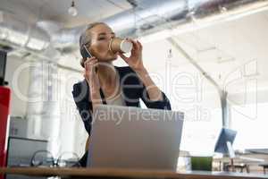 Businesswoman having drink while talking on phone at table