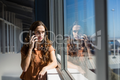 Businesswoman talking on mobile phone by window at office