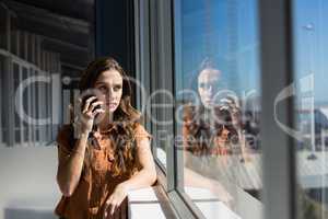 Businesswoman talking on mobile phone by window at office