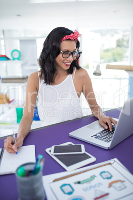 Smiling executive writing in diary while using laptop