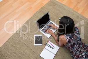 Female executive using laptop while lying on carpet