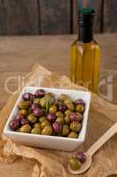 Olives with rosemary served in bowl by oil bottle on table