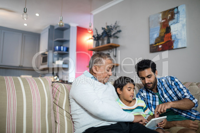 Father and grandfather pointing on tablet used by boy