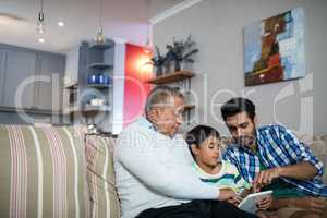 Father and grandfather pointing on tablet used by boy