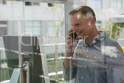 Smiling fashion designer talking on mobile phone seen through glass