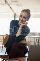Happy businesswoman with hand on chin sitting on chair in office
