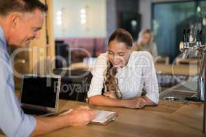 Manager and bartender discussing over clipboard in bar