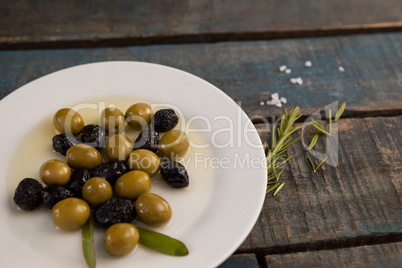 Green and dry black olives with oil in plate on table