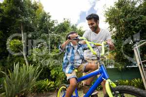 Happy father assisting son for cycling