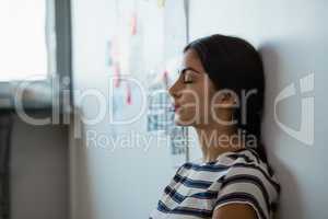 Tired woman leaning on wall in office