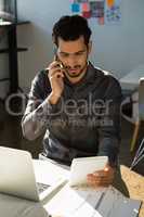 Man talking on mobile phone while using tablet at office