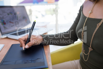 Female graphic designer using graphic tablet at desk in the office