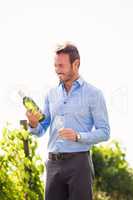 Smiling man holding wine bottle and glass against sky