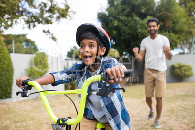 Boy cycling with father standing in background