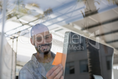 Smiling designer using computer seen through glass