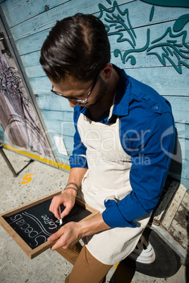 Owner writing menu while sitting by food truck