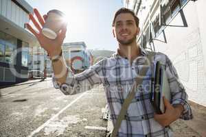 Young man holding disposable cup gesturing while walking by building