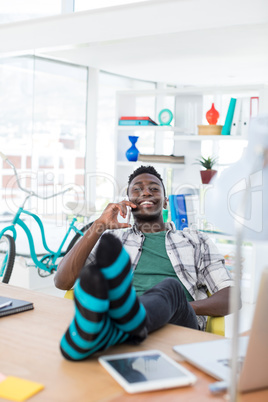 Male executive talking on mobile phone while relaxing at his desk in office