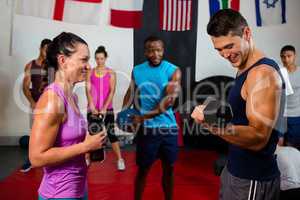 Smiling woman looking at male athlete lifting dumbbell