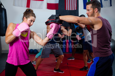 Female boxer and instructor practicing with boxing