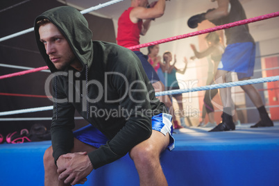 Young male boxer sitting on boxing ring at fitness studio