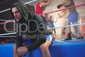 Young male boxer sitting on boxing ring at fitness studio