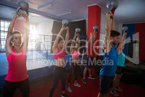 Young athletes lifting kettles against boxing ring