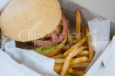 Hamburger and french fries in a take away container on table