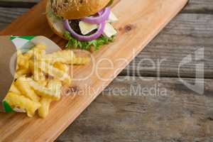 High angle view French fries in box by burger on cutting board