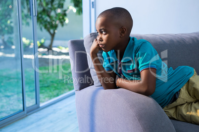 Thoughtful boy looking away while sitting on sofa