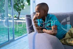 Thoughtful boy looking away while sitting on sofa
