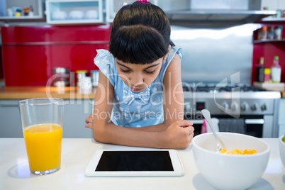 Girl looking at tablet computer while sitting with breakfast