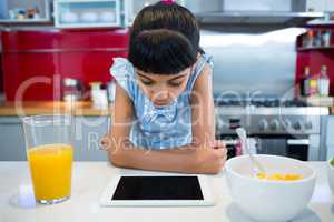 Girl looking at tablet computer while sitting with breakfast