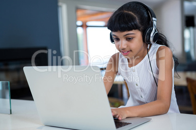 Girl listening music from headphones while using laptop