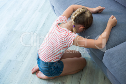 Sad girl kneeling by sofa at home