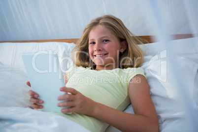 Portrait of girl holding tablet computer while lying on bed