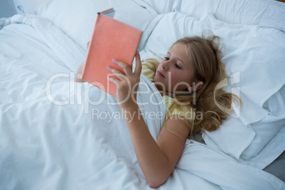 Girl reading book while lying on bed