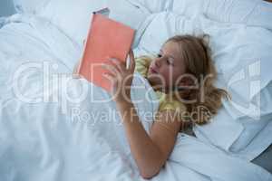 Girl reading book while lying on bed