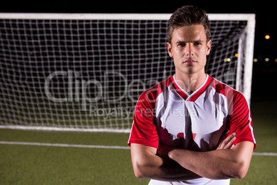 Confident male soccer player standing with arms crossed against goal post on field